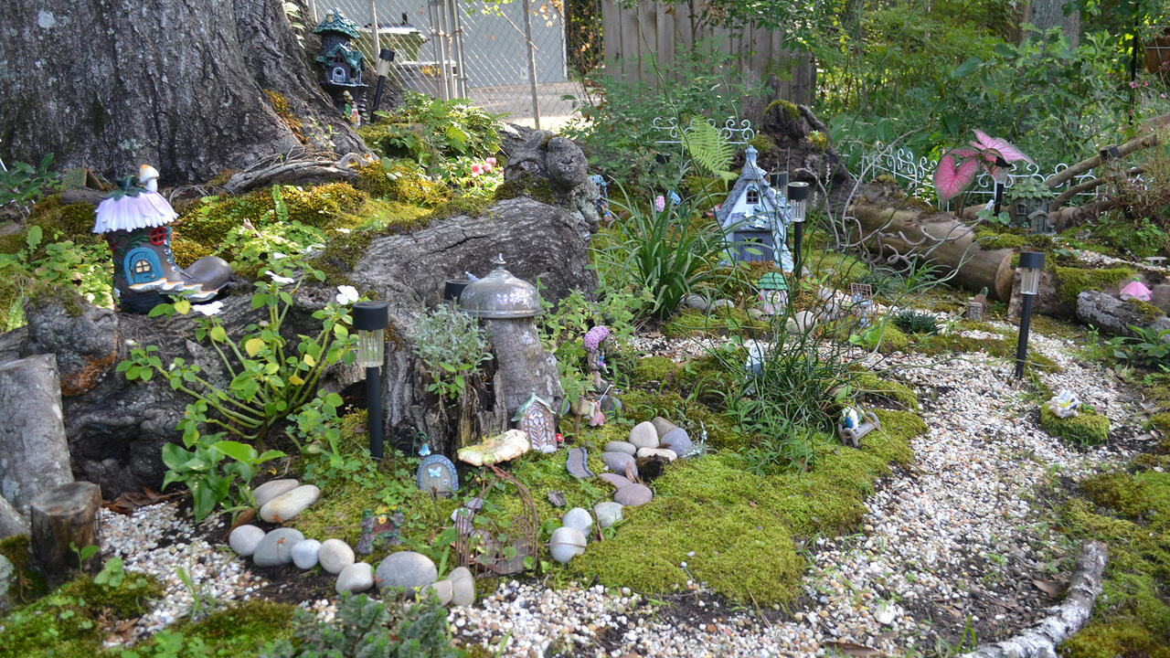 A pea gravel trail surrounds a miniature fairy village under a tree.
