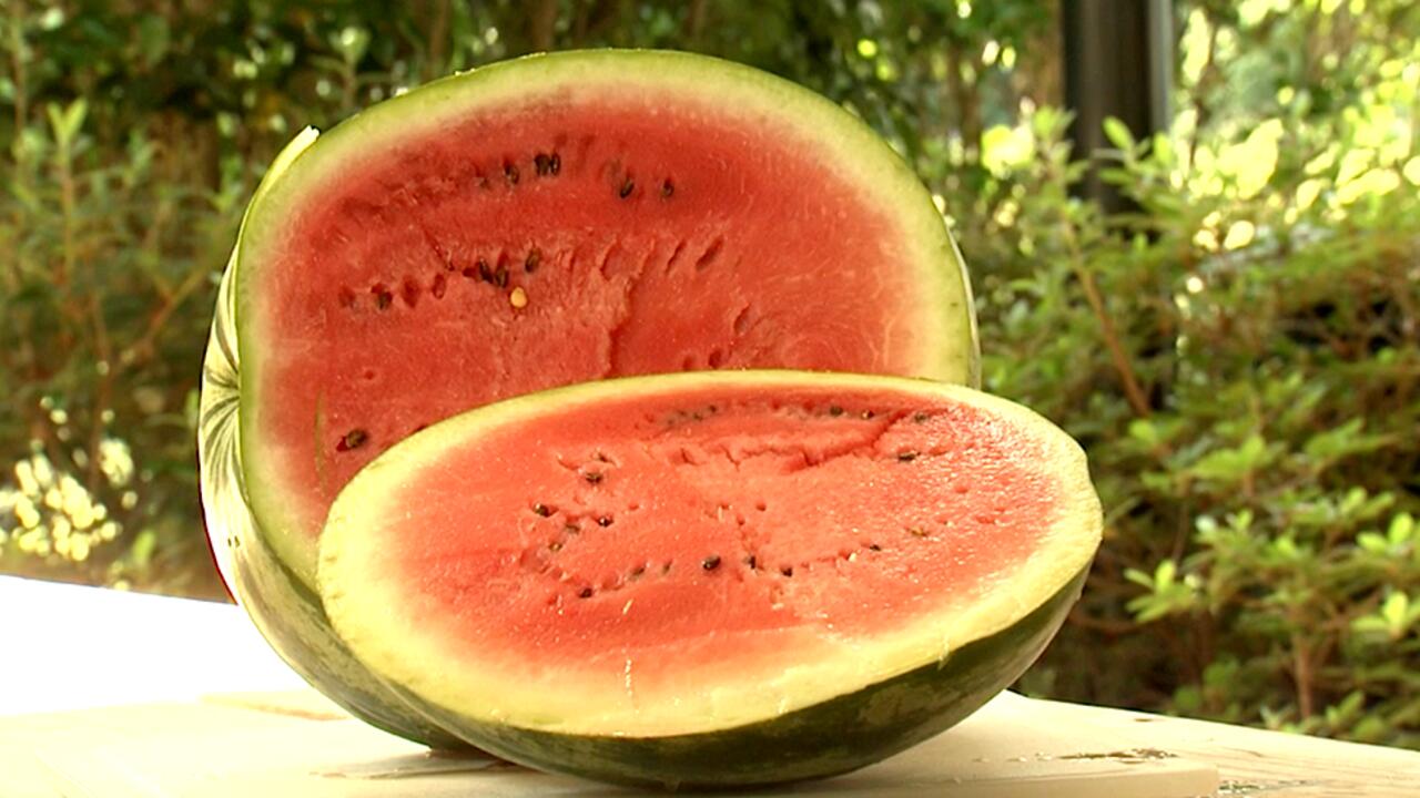 A sliced, ripe watermelon sits on a table outdoors.