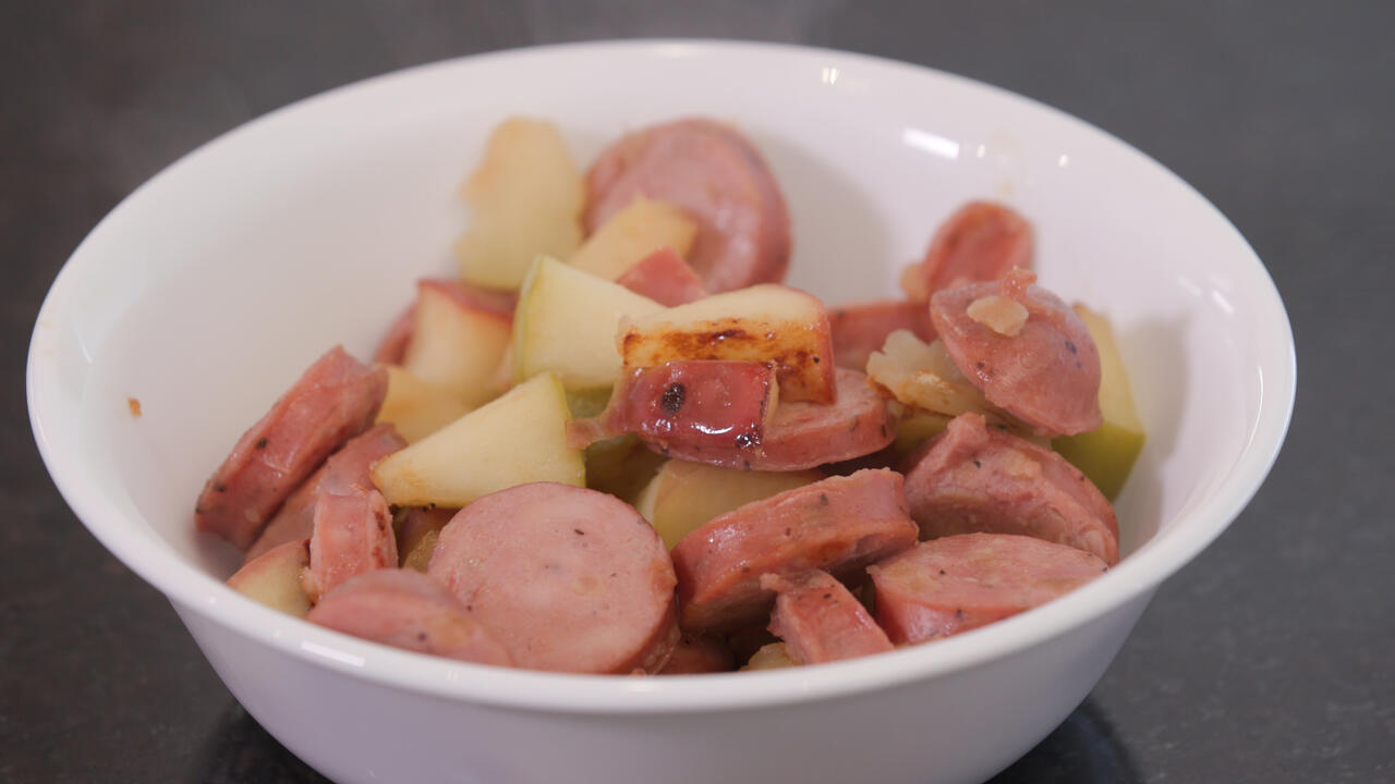 A bowl of cooked sausage and apples.