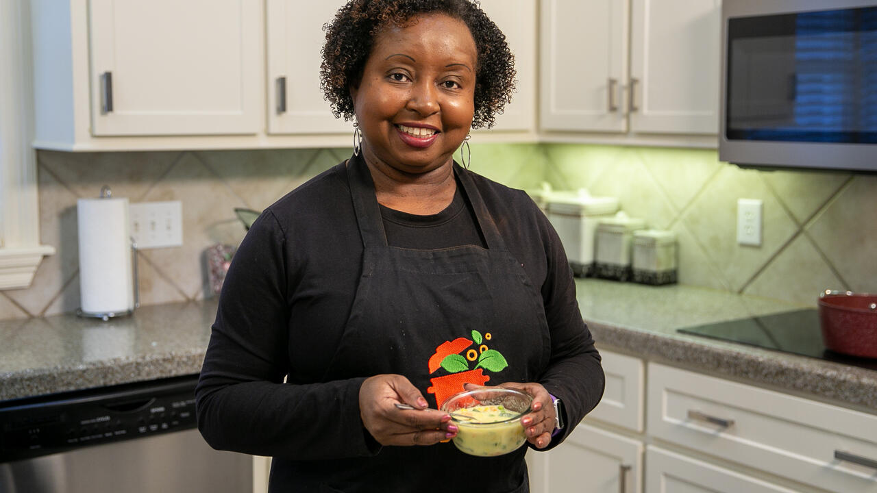 A woman stands in a kitchen and holds a bowl of soup.