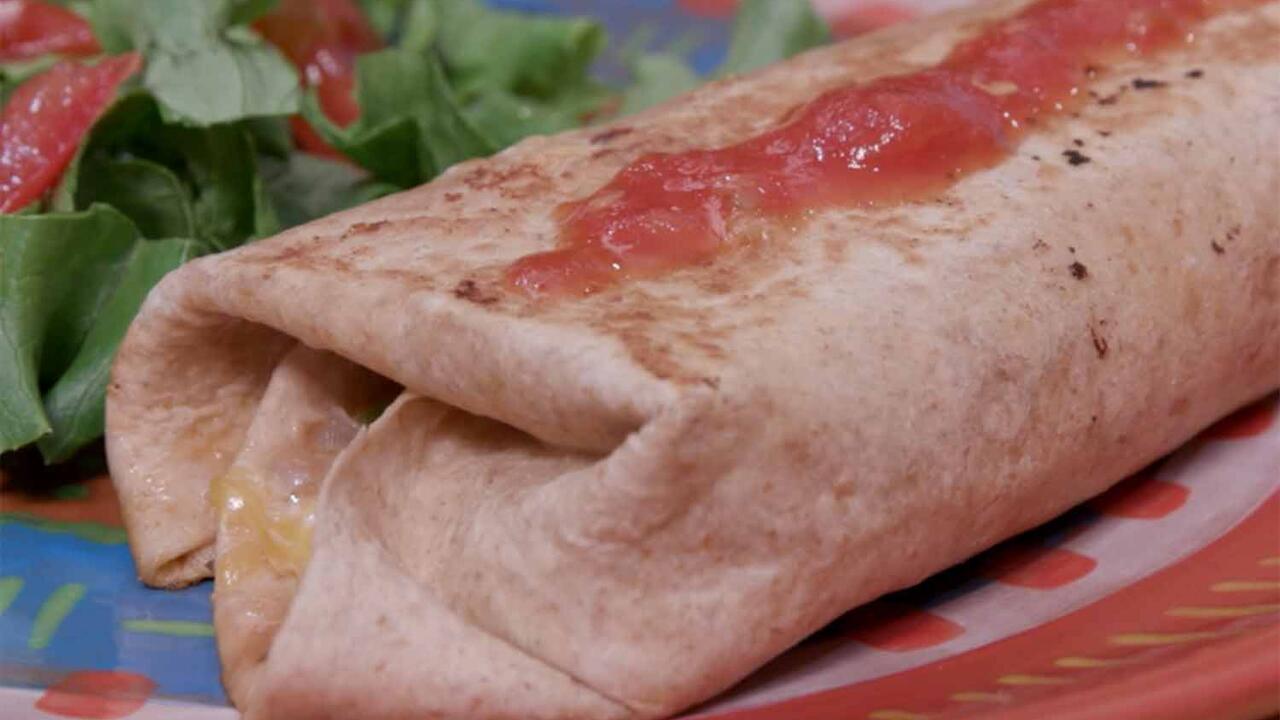 A grilled burrito topped with salsa and a green salad with tomato served on a multicolored plate.