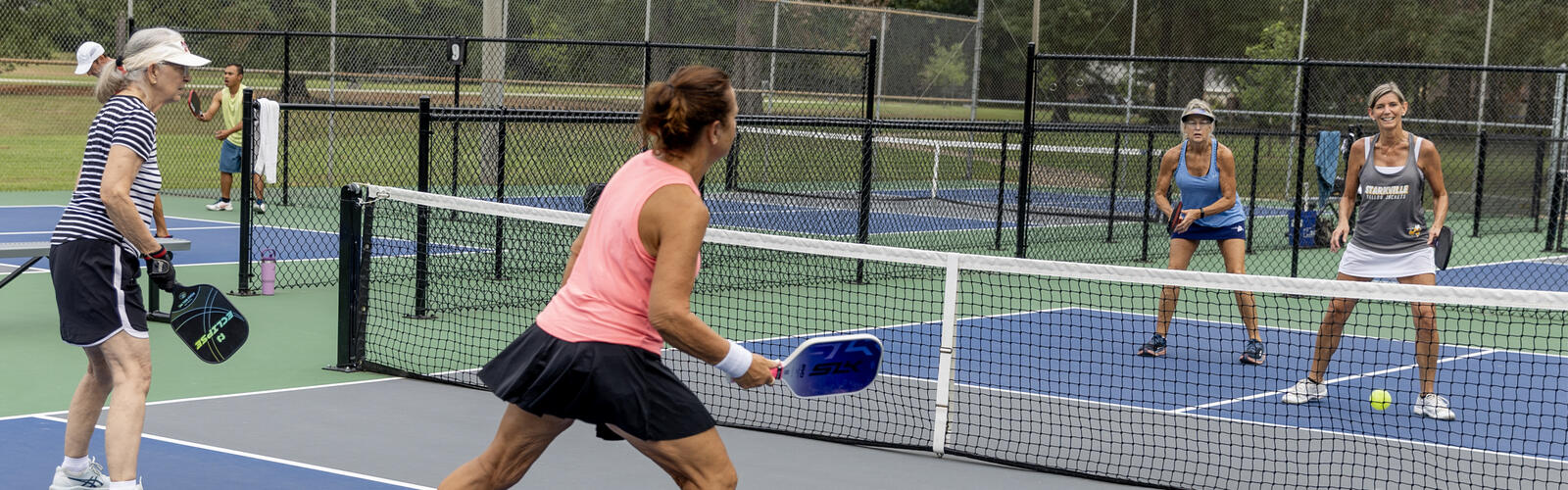 Four women holding paddles play a game on a court.