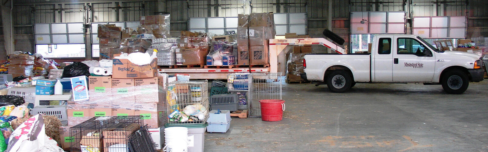 A white pickup truck inside a warehouse with boxes of household items behind it.