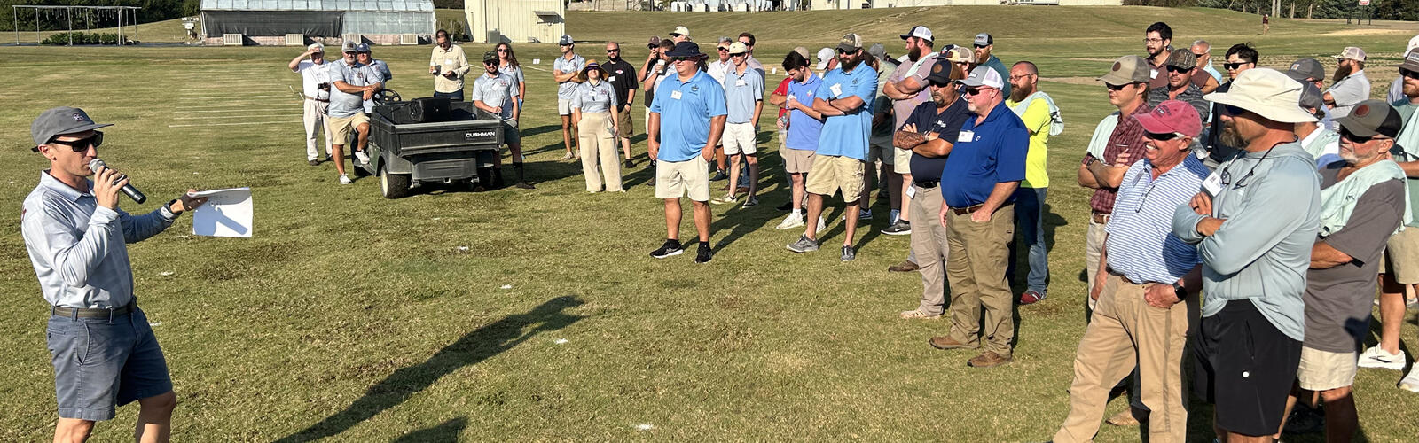 A presenter shows turf samples to a crowd of onlookers.