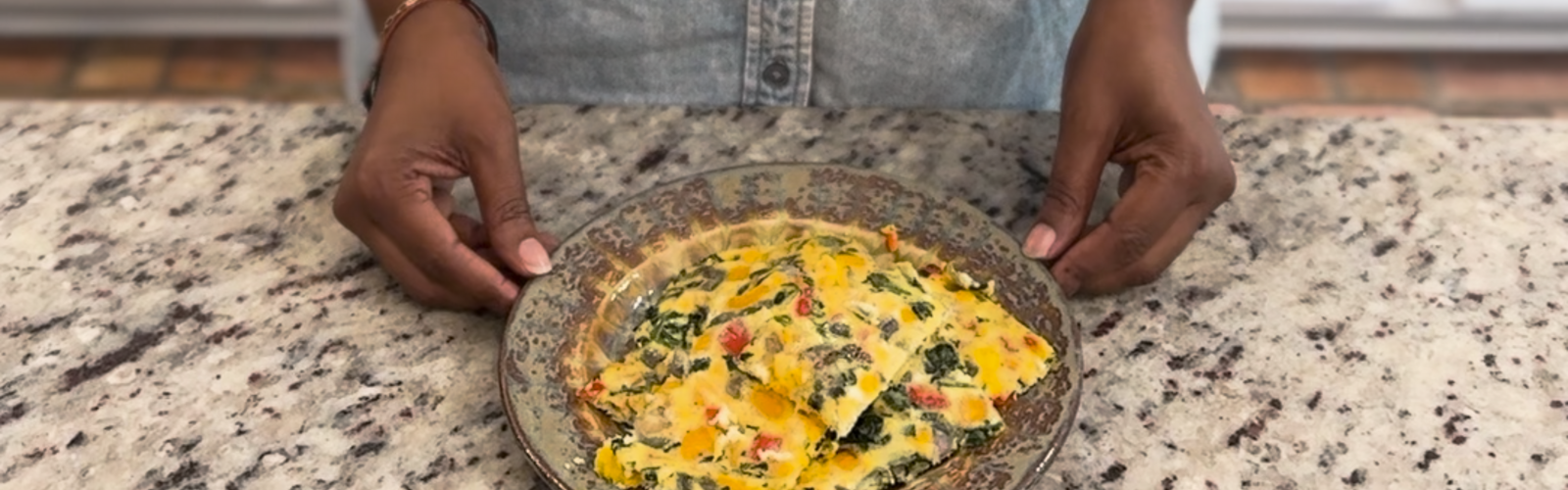 A woman stands at a kitchen counter with a plate of Sheet Pan Eggs and Veggies.