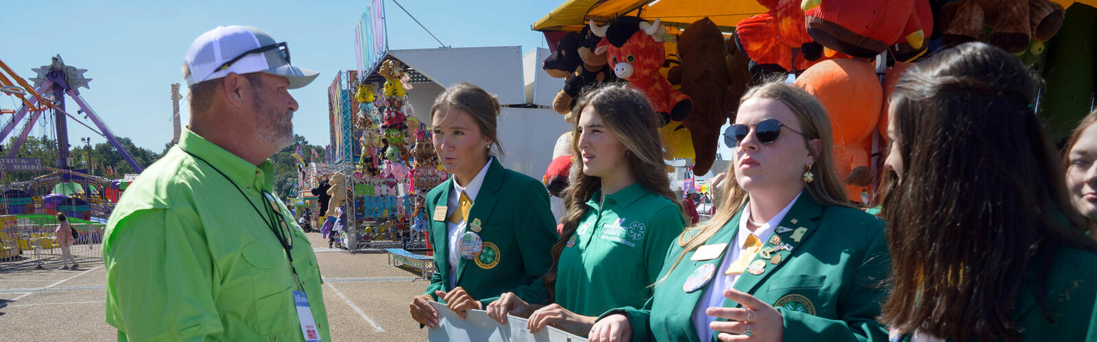 A person wearing a green polo talking to young people wearing green and holding a Walk Mississippi banner