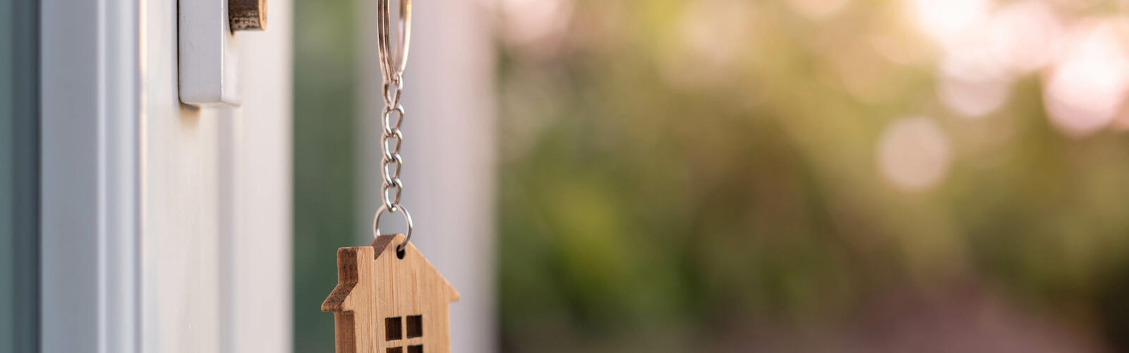 A house key on a house-shaped keychain is insterted in the front door lock of a home.