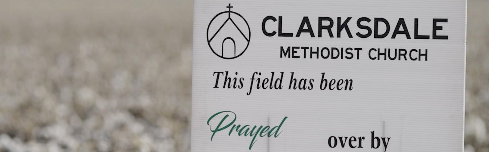 A small, white sign stands in field displaying the words, “This field has been prayed over by Clarksdale Methodist Church.”