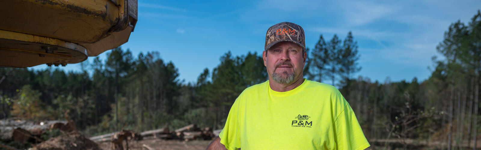A smiling person standing next to a bulldozer at a logging site.