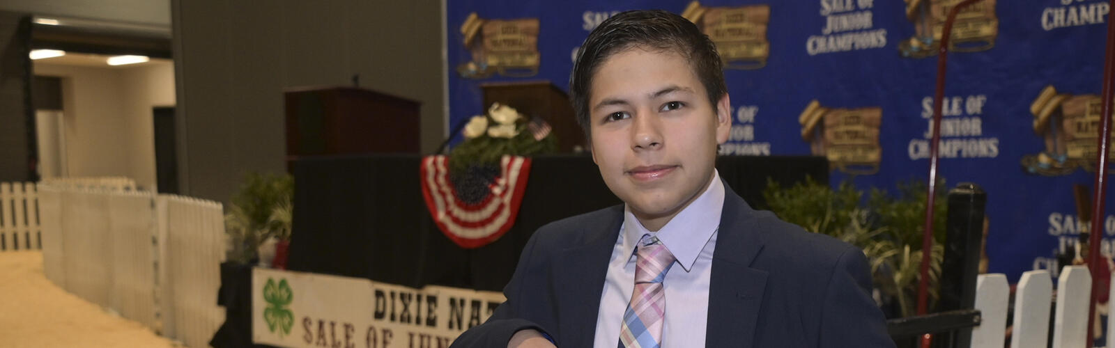 A person in a blazer and tie leans on a fence inside the Dixie National Sale of Junior Champions arena.