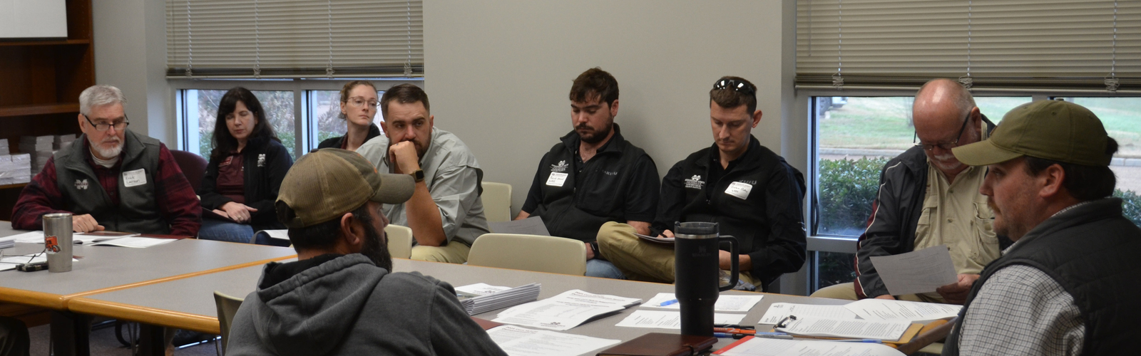 A man sits at the end of a conference room table with others gathered around.