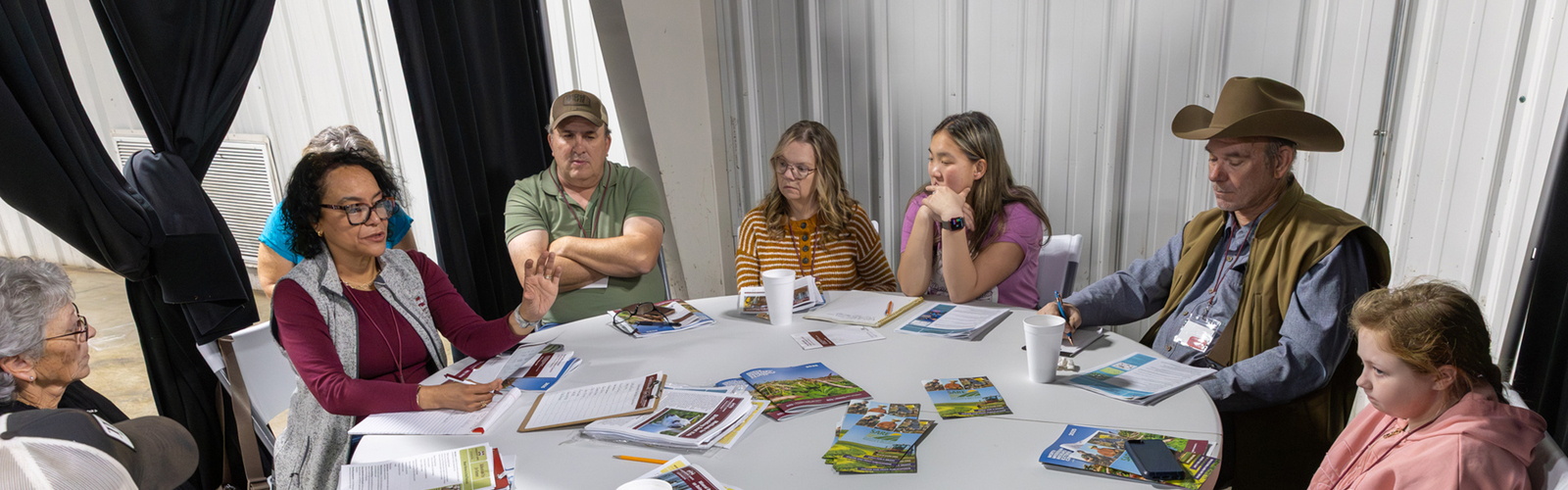 A circle of people sit in a meeting around a table.