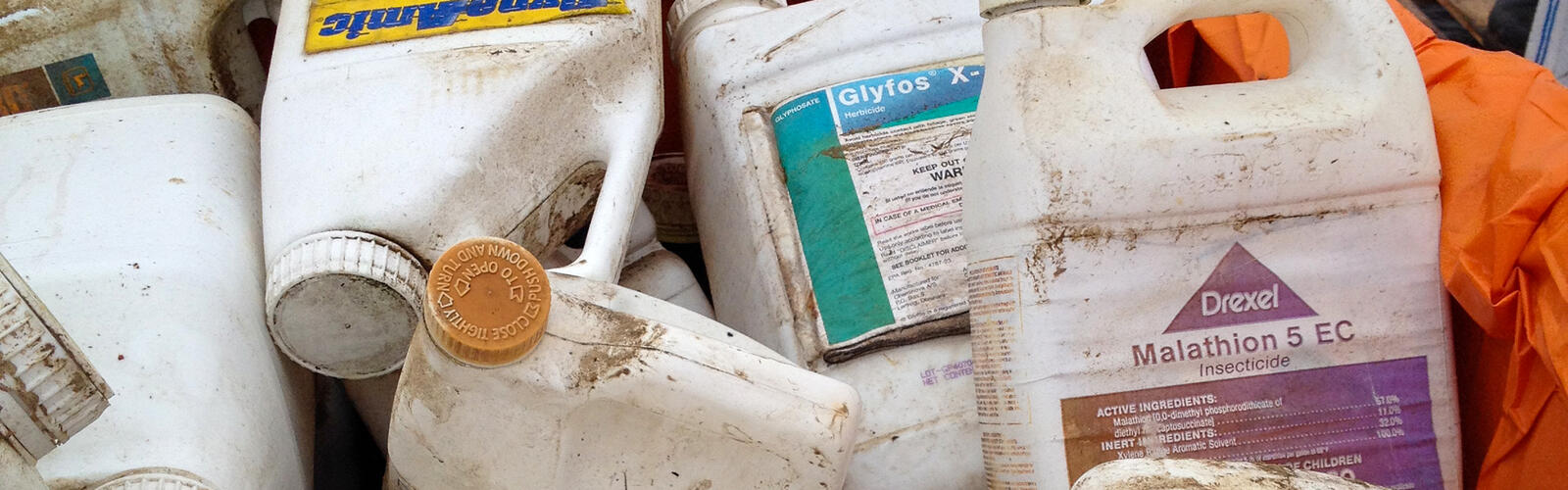 Pile of used agricultural chemical containers in an orange-lined bin.