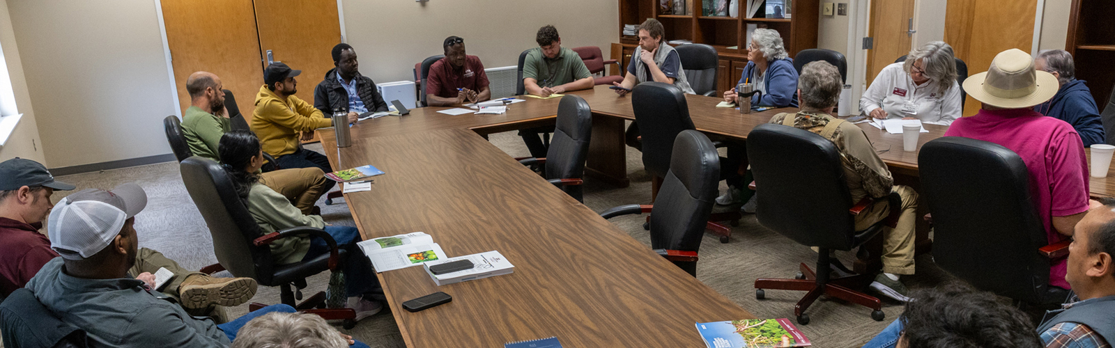 A large group of people seated around a table in a conference room.