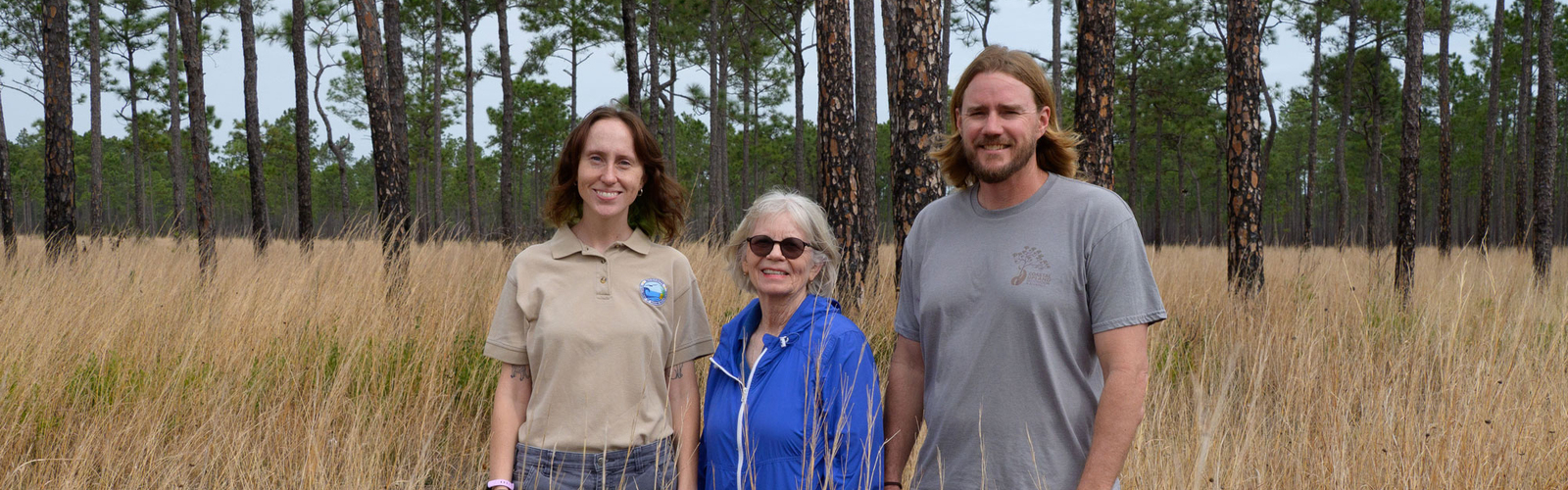 Three people standing amid tall grass and smiling.