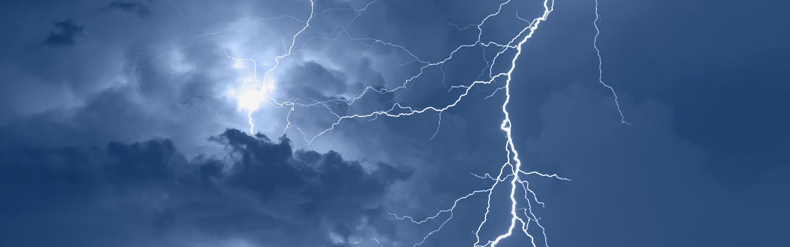 Lightning stirkes light up a cloudy, blue night sky.