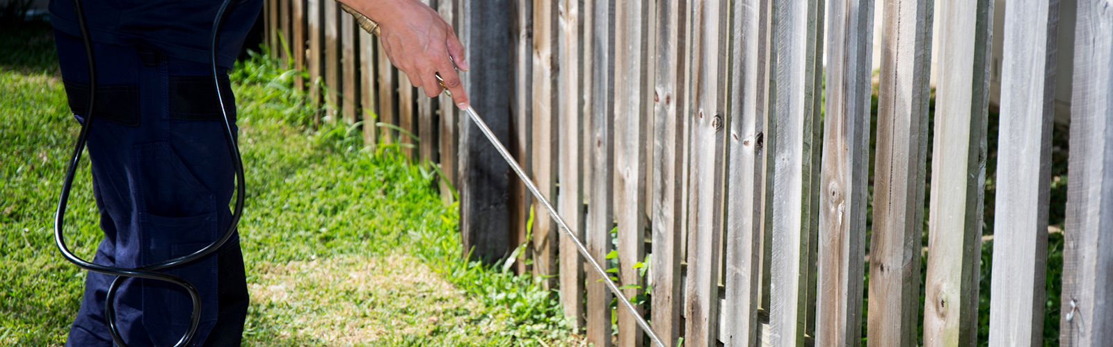 A person uses a wand to spray a fence outdoors.