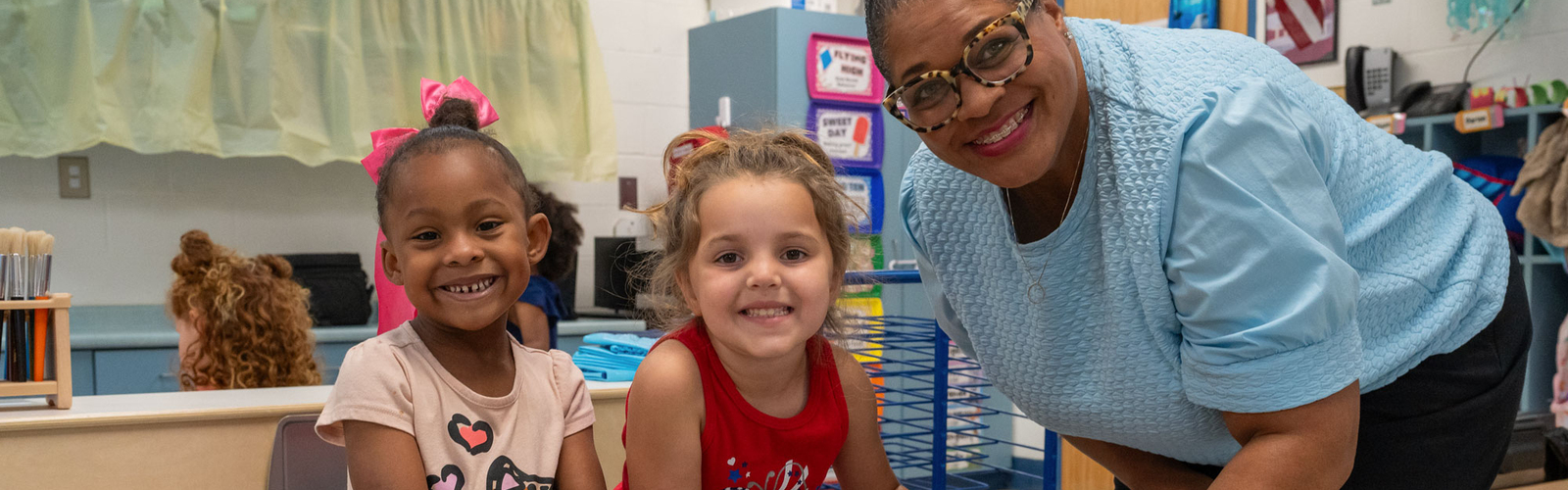 A smiling adult with two smiling children at a bead and building station.