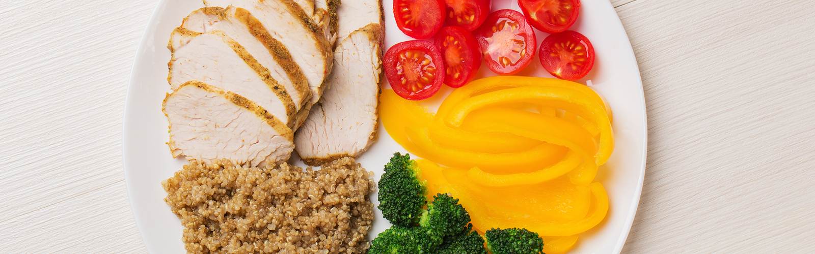 A plate with tomatoes, yellow peppers, broccoli, quinoa, and chicken.