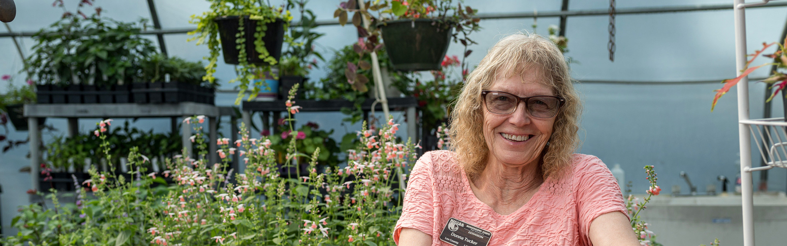 A person smiling in a greenhouse surrounded by colorful foliage.