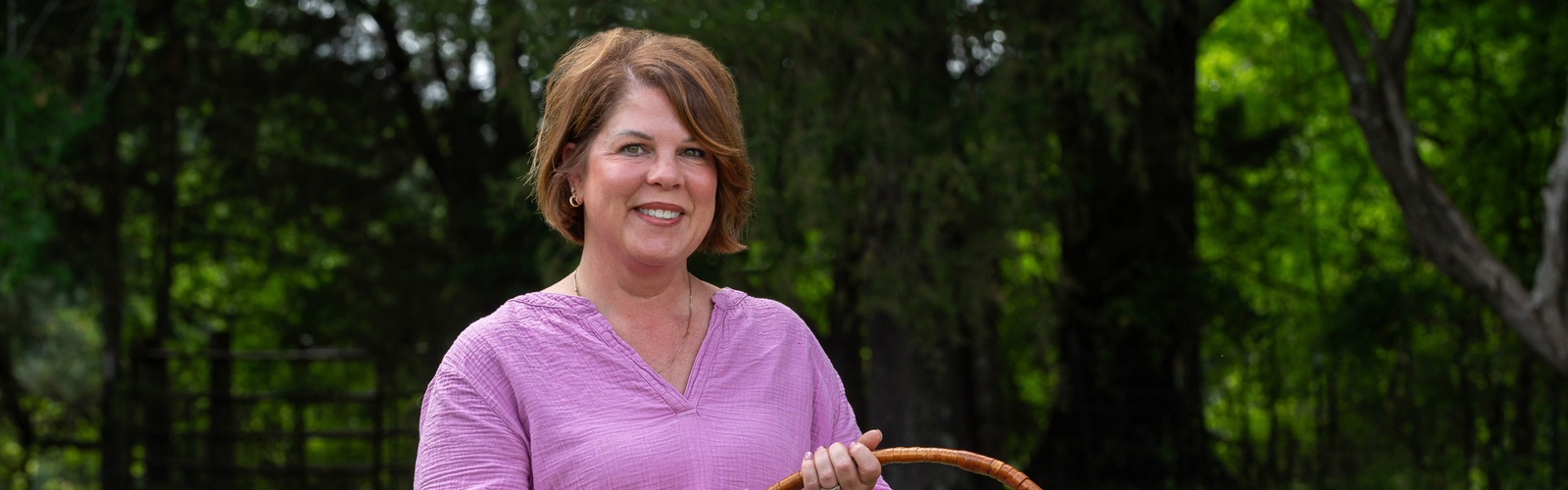 A smiling person standing outside and holding a basket full of colorful flowers.