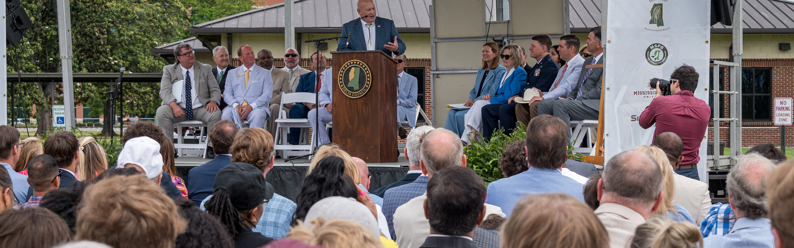 A man speaks to a large crowd from an outdoor stage.