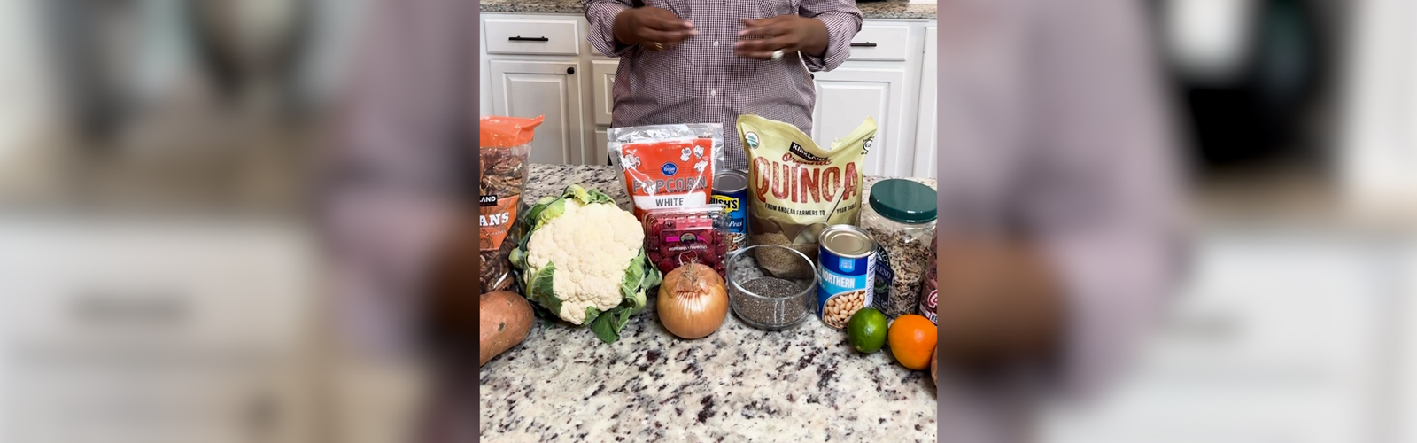 A woman stands behind a kitchen counter with several examples of fiber-rich foods displayed.