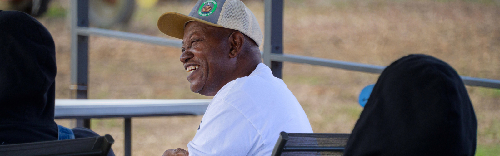 A seated man wearing a baseball hat and smiling.