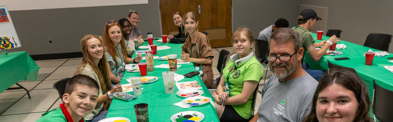 Teens smiling with an adult at a table full of painting supplies.