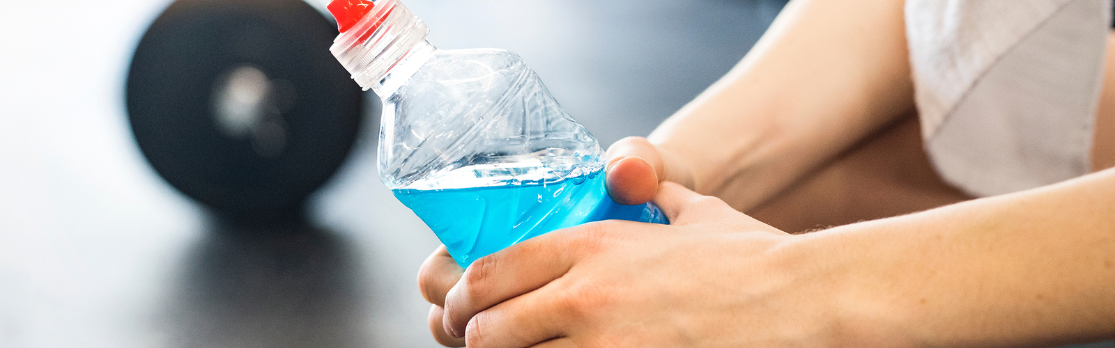 Closeup of hands holding a blue sports drink after a hard workout in the gym.