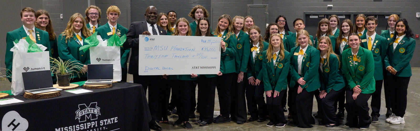 A large group of teenagers pose for a photo with a man holding a large presentation-style check.