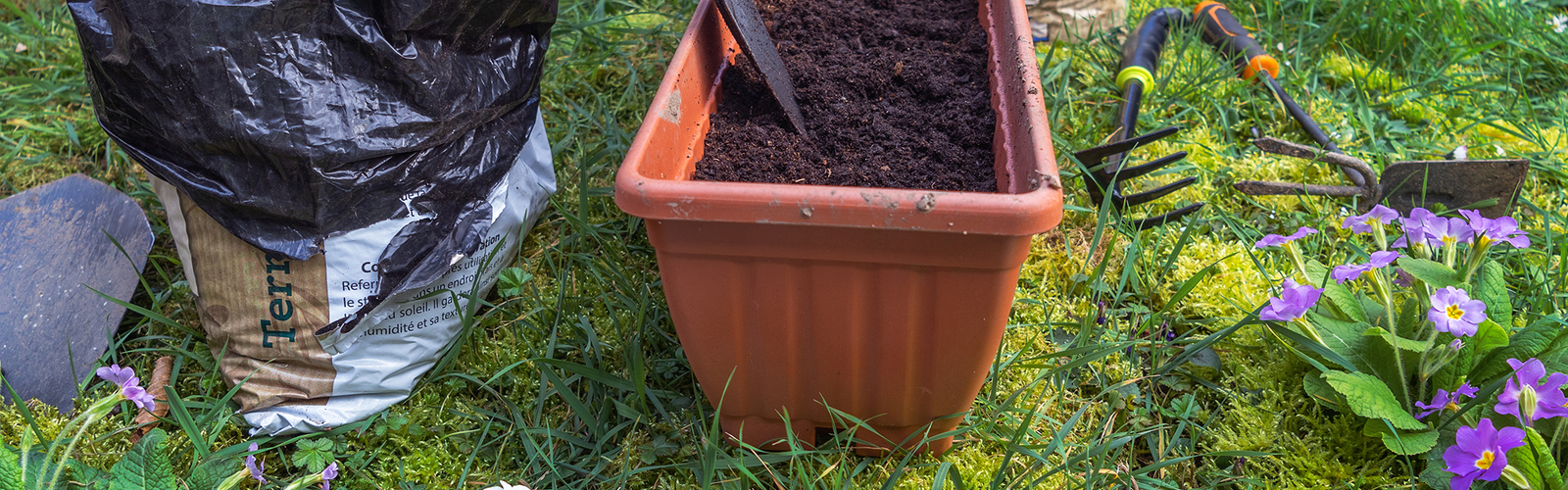 Woman mixing potting soil with a trowel in a pot on a lawn.