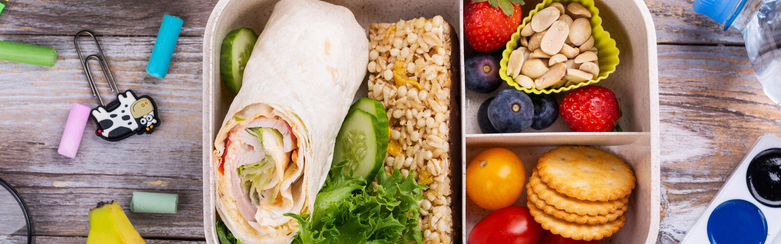 School lunchbox packed with nutritious foods surrounded by colorful school supplies