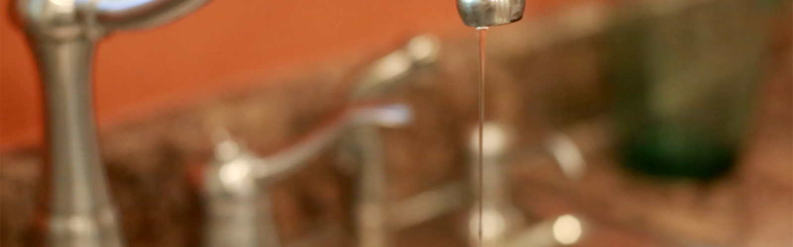 A thin stream of water drips from a stainless steel kitchen sink faucet.