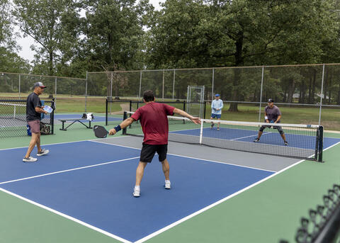 Four men holding paddles play a game on a court.