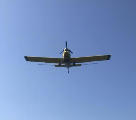 Crop plane flying high in a clear blue sky.