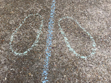 Two chalk outlines of feet positioned on opposite sides of a blue chalk line on pavement.