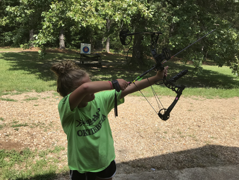 Young archer with the bow raised slightly above shoulder height, front arm straight with the elbow turned in a bit, and drawing arm pulling the string back. 