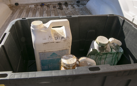 A large, plastic container holding smaller containers with signs of leaking.