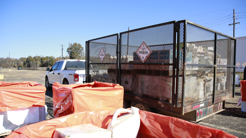 A pickup truck with a large, enclosed trailer sits at a collection location. The trailer has hazard placard with the word "POISON."