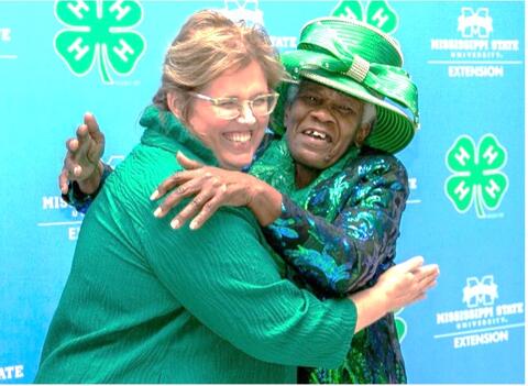 A lady with a green 4-H hat gives a hug to another lady in 4-H green
