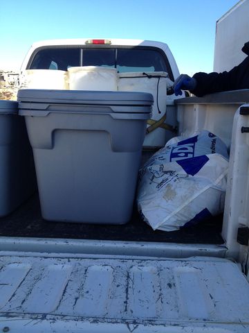 A pickup truck bed with plastic storage bins and a bag of absorbent material.