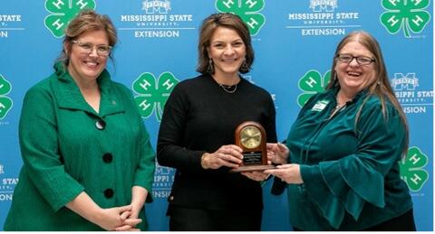 Two women present another woman with the Kenneth Cook Award