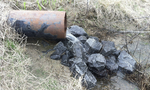 Water flows out of a rusted pipe onto large rocks.
