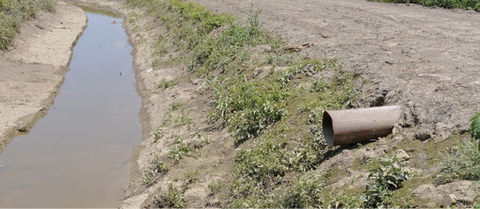 A ditch with a horizontal pipe coming out from the ground on the right.