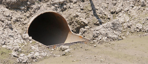 Close-up of a large slotted inlet pipe opening installed at the edge of a crop field.
