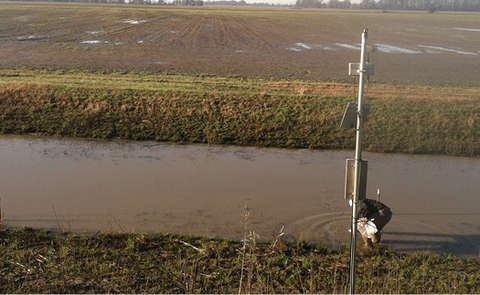 TWR ditch in spring (March). The ditch is full of water, and the surrounding field is brown and green.