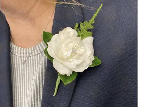 A close-up of a gardenia flower and foliage pinned to a person’s lapel.