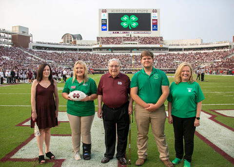 A group of five men and women standing on the MSU football field during a game day.