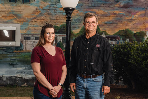 A woman and a man standing in front of a mural and lamppost.